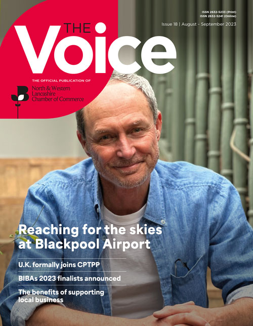 MAgazine Cover for the Voice. White man in a blue shirt sat on a chair smiling.